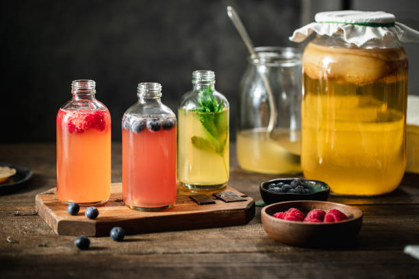 Flavored kombucha tea bottles in the kitchen with ingredients on wooden table. Raspberry, blueberry and mint flavored fermented drinks.